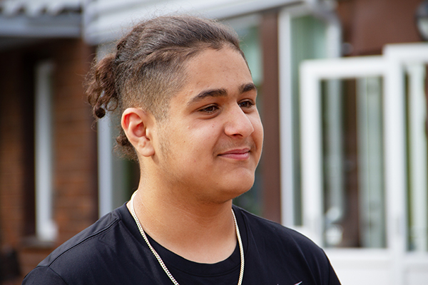 Kille i övre tonåren med svart hår som är kort på sidorna, det längre håret är uppsatt i en tofs bak på huvudet.