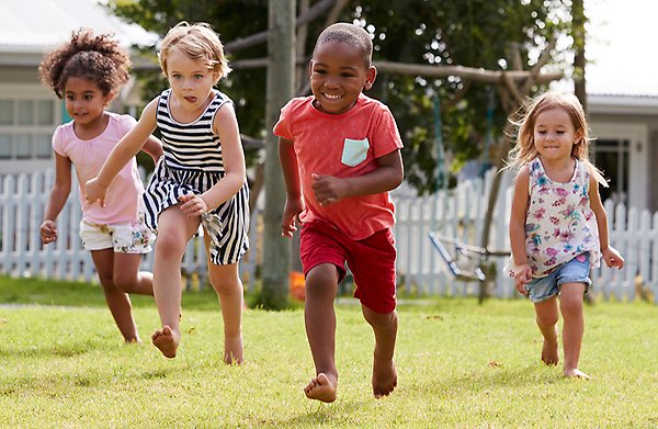 Fyra barn springer barfota på en gräsmatta.