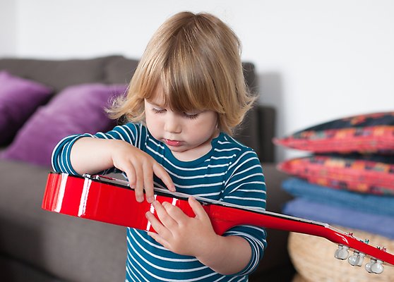 Litet barn spelar på en röd gitarr.