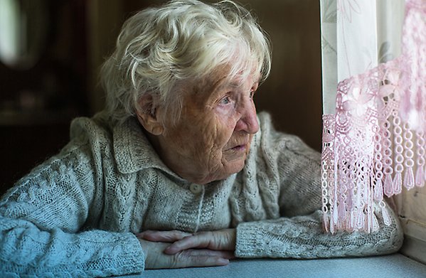 Äldre dam tittar ut genom ett fönster.
