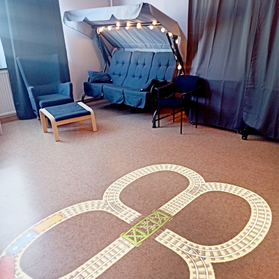 Rum med soffa, fåtölj och fotpall. På golvet finns en tågräls projicerad, en interaktiv Tovertafel.