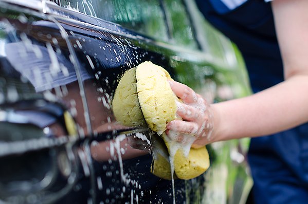 Hand med tvättsvamp som tvättar en bil