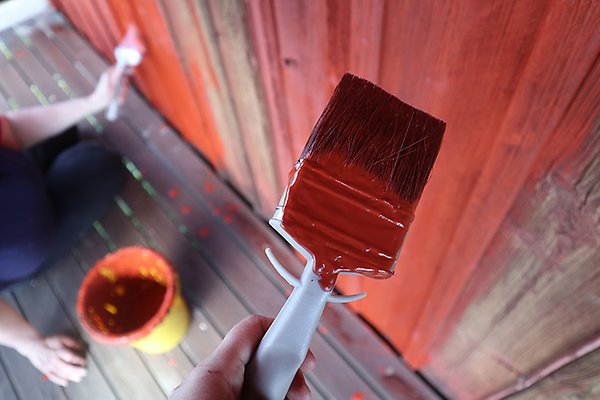 Pensel som målar en fasad med röd färg