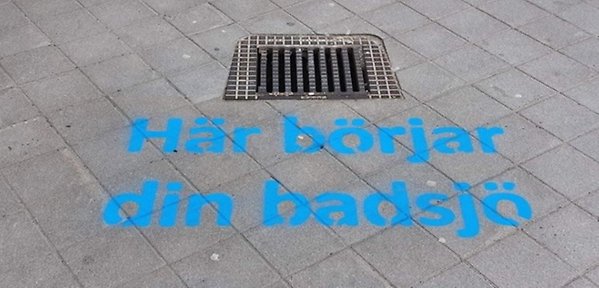 Gallerbrunn med texten Här börjar din badsjö, spraymålad med blå färg på marken