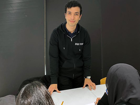 Pedram stöttar två elever med läxläsning.