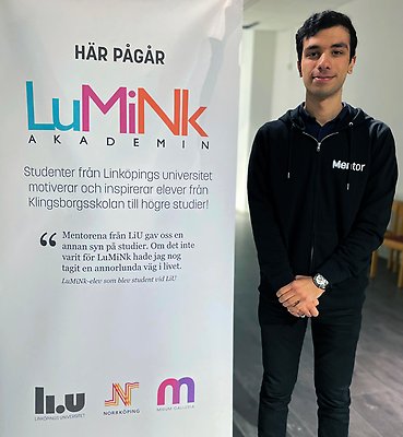 Pedram står bredvid en rollup som beskriver LuMiNk:s verksamhet